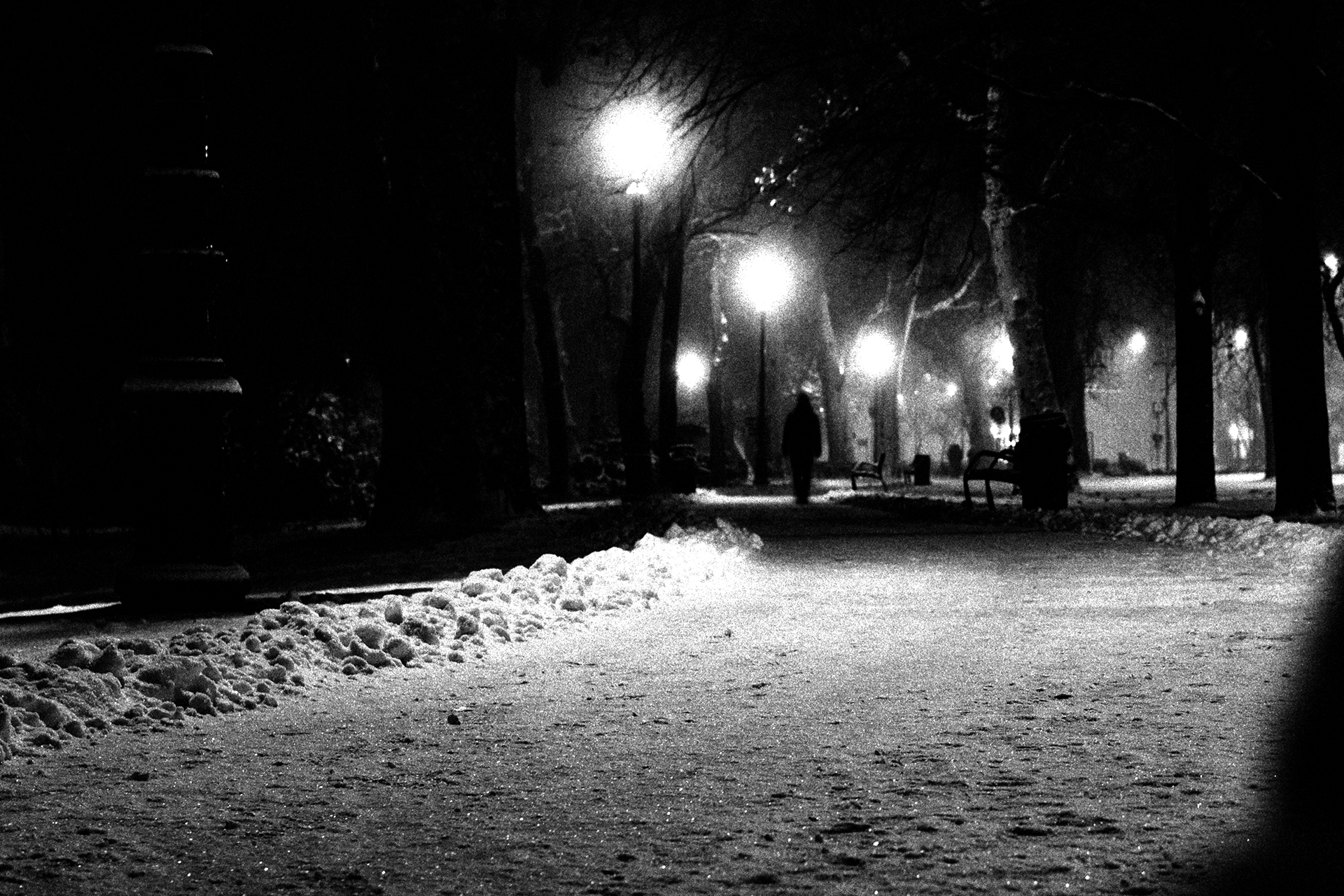 A solitary figure walks a lit path on a dark and snowy night