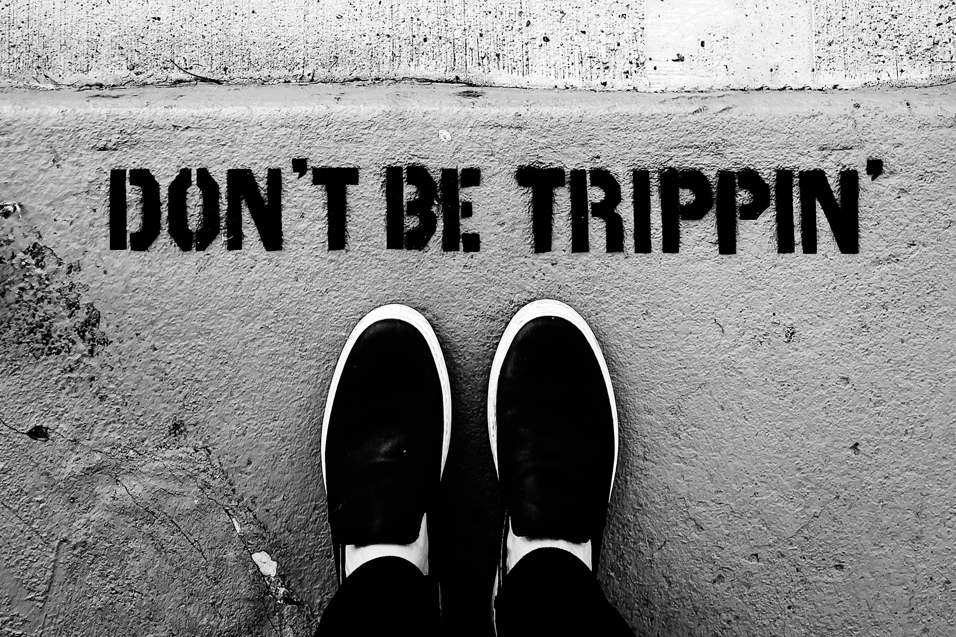 Looking down at two feet pointed at the phrase “Don’t be Trippin’” painted on the pavement