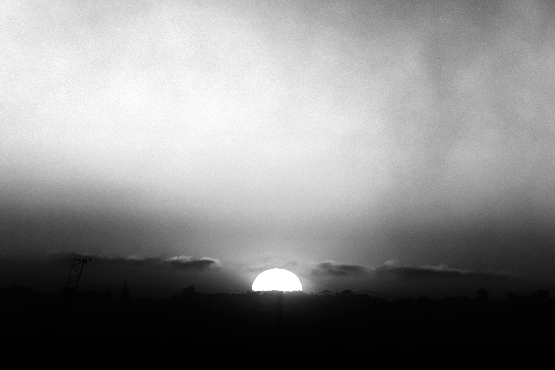 The sun rising through the clouds and over a distant hill